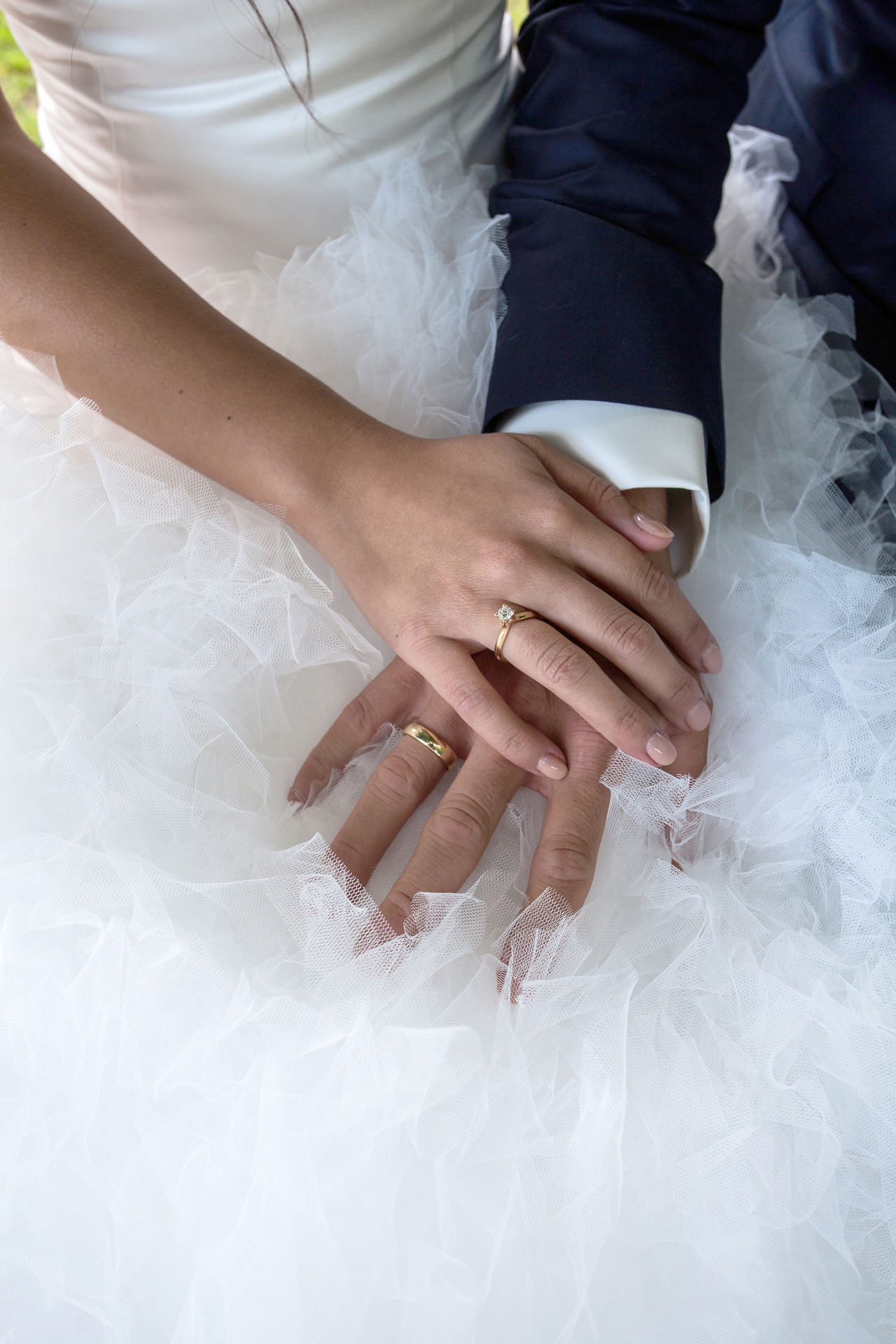 En kvindehånd med en vielsesring og en mandehånd med en vielsesring med en bryllupskjole som baggrund