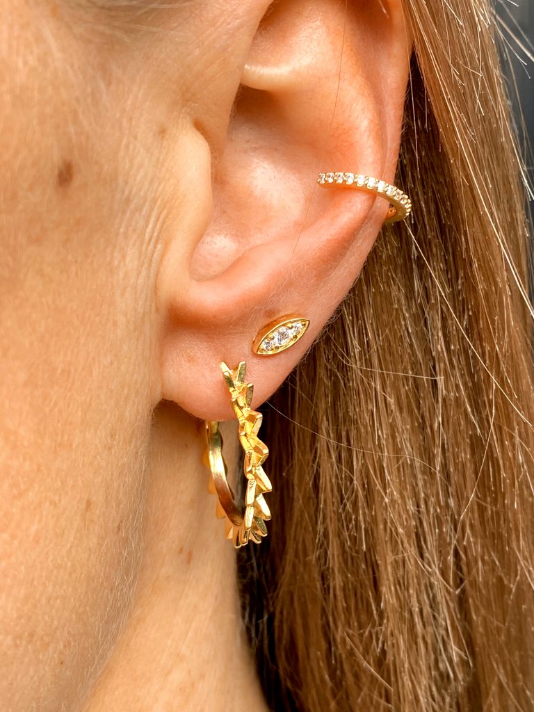 Kvindeligt øre med tre forskellige guldøreringe med diamanter i. 

